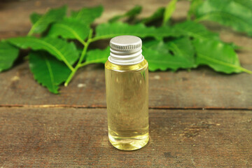 Neem oil in bottle and neem leaf on wooden background. Neem oil is an excellent moisturizing oil and contains various compounds that have insecticidal and medicinal properties.