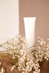 White bottles of cosmetics with flowers on a brown background. Cream Tube, Advertising Template.