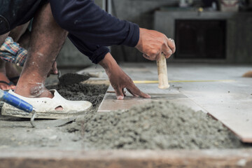 Motion blurred hand of worker installing the floor tile by wooden hammer at the construction site