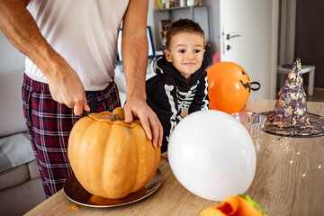 Fototapeta premium Getting ready for Halloween. Happy family father and children cut pumpkin for holiday of halloween. Father and little son have fun and celebrate Halloween at home