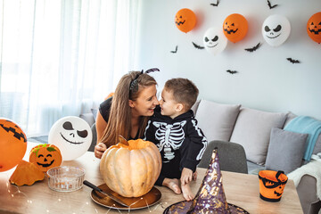 Happy family a cheerful woman and her son are laughing and getting ready for Halloween by carving a pumpkin jack o lantern. Mother with her son prepare pumpkin for halloween in the kitchen