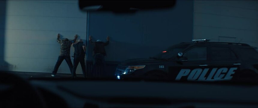 WIDE Police officer searches two suspects in the street at night. Police car lights flashing in the background. Shot with RED cinema camera and 2x Anamorphic lens
