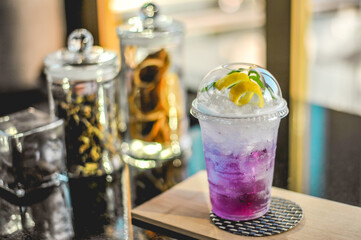 A Signature purple drink made from butterfly pea flower and decorated with lemon peel twisted and mint leaf in a plastic takeaway cup 