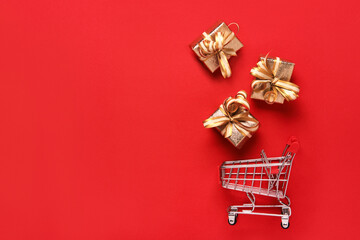 Golden gifts boxes and shopping cart on red background. Black friday sale and shopping day concept