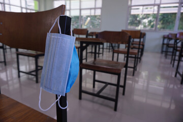 The medical face blue mask hangs on the wood lecture chairs in the empty classroom. Concept during the germs, coronavirus disease COVID-19 outbreak and pandemic in the 2020s. Back to school concept.