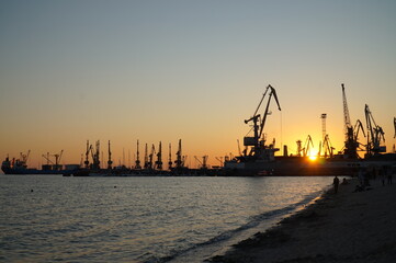 Silhouettes of cranes and ships against the setting sun.