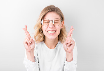 Pleased cheerful blonde woman puts all efforts in wishing good luck, crosses fingers, has faith for better, isolated over white background