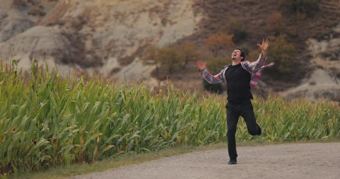 Happy Caucasian man jumping for joy in slow motion as he runs down a country lane next to a corn field at sunset. Personal achievement goal, drunk of life, freedom in nature, Feeling successful.