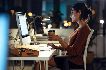 Beautiful young business woman working with computer while drinking coffee sitting in the office.