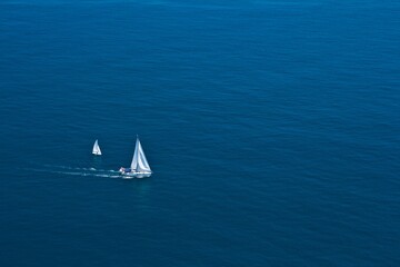 Aerial view on two white sailboats leaving wake in the blue Mediterranean sea .