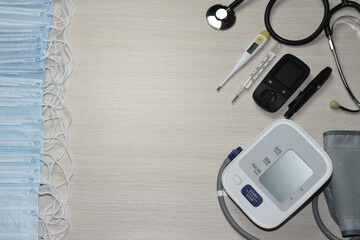 On a light beige background are medical masks, a tonometer, electronic and mercury thermometers, a glucose meter with a Lancet, and a stethoscope.
