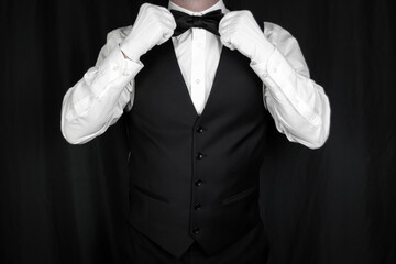 Portrait of Butler or Waiter in Black Vest and White Gloves Straightening Bow Tie. Concept of Service Industry and Professional Hospitality. Dependable Servant. Copy Space for Service.