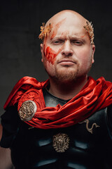 Headshot of serious legionary with bald head and black armour with red cape in dark background.
