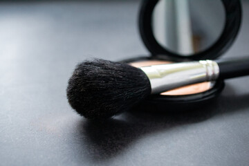 A black makeup brush on an open box with a mirror and powder puff and pink powder. Black...