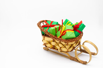 Fototapeta premium Old-fashioned wicker Santa sleigh with Christmas gifts wrapped in green paper with red ribbon. Copy space