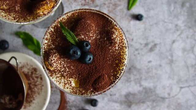 Traditional Italian tiramisu cake sweet dessert with blueberries, mascarpone cheese and espresso coffee in a glass cup