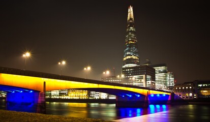 LONDON - MARCH 15 2014: Lit up with yellow and blue lights bridge over the Thames river in front of the Shard skyscraper at night in London.
