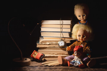 Old retro doll toy and stack of books on the table in the dark background.