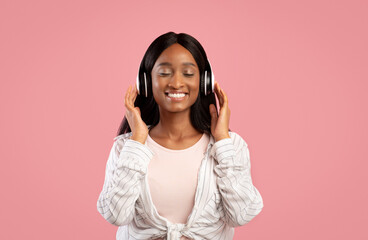 Portrait of smiling back woman listening to her favorite music with closed eyes, pink studio background