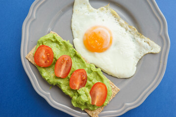 Simple and delicious breakfast: fried eggs on rye bread with guacomole, avocado puree and cherry tomato slices. 