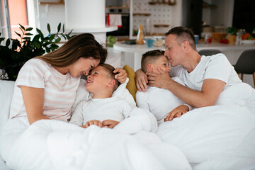 Fototapeta premium Young family enjoying in bed. Happy parents with sons relaxing in bed.