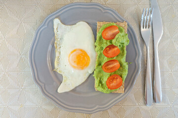 Simple and delicious breakfast: fried eggs on rye bread with guacomole, avocado puree and cherry tomato slices. 