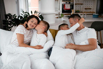 Young family enjoying in bed. Happy parents with sons relaxing in bed.