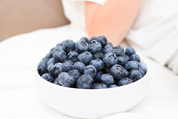 A bowl of tasty blueberry standing on a bed near the person for breakfast