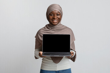 Cheerful African Muslim Woman In Hijab Holding Laptop With Blank Black Screen