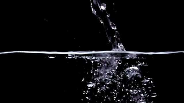 A jet of water pouring onto the water surface in slow motion on a black background.