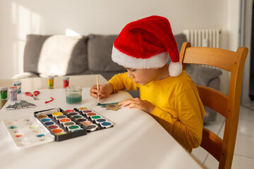 child in santa hat, occupation and activity for small children before christmas, boy learning drawing at home,