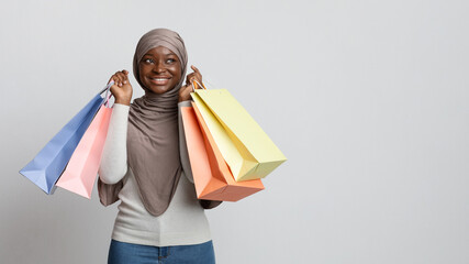 Happy black muslim shopaholic woman in hijab posing with lots shopper bags
