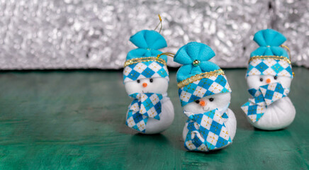 Group of three Christmas snowmen on a green wooden table with an unfocused light background