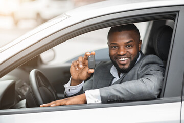 Happy black guy in suit holding key from new car