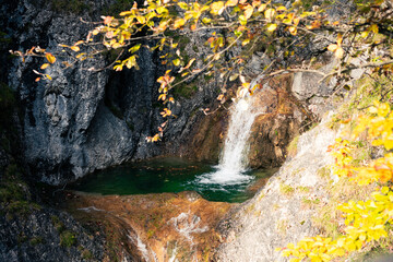 A picture of a turquoise colored small waterfall surrounded by autumn colored trees
