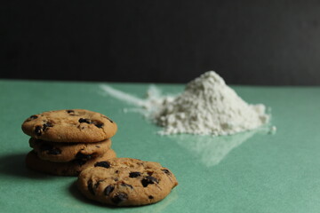 two or more cookies with chocolate drops are lying next to each other and a hill on a green grass background behind in the background is a hill of flour or powdered sugar there is a copy space
