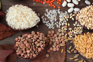 Uncooked dry cereal food group in wooden spoons on wooden background with autumn leaves.Selected  rice and lentil cereal spoons