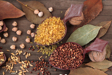 Uncooked dry cereal food group in wooden spoons on wooden background with autumn leaves.Selected two cereal spoons