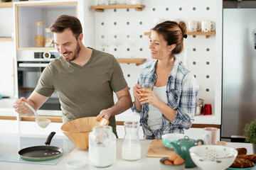 Husband and wife making pancakes at home. Loving couple having fun while cooking.