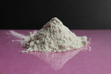 white flour of the highest or first grade lies in a heap on a black and pink fuchsia mirror background with a reflection side view there is a copy space