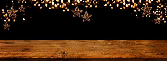 Golden Christmas stars with festive bokeh lights in front of illuminated rustic wooden table. Background for christmas and new years concepts. Space for text and design.