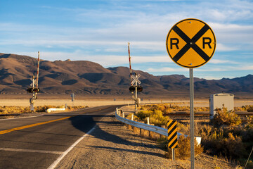 Image of a railroad crossing at the intersection of a highway in a mountainous desert
