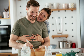 Husband and wife making pancakes at home. Loving couple having fun while cooking.