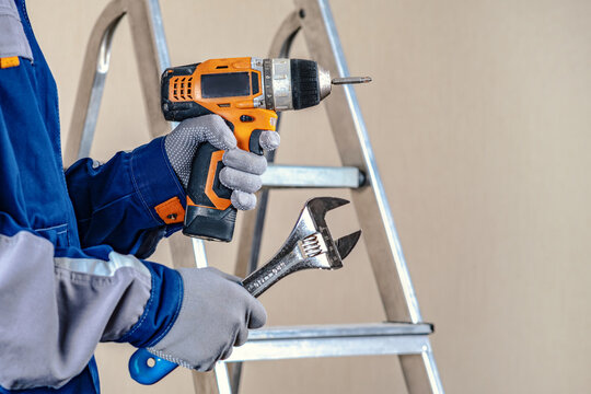 The master is holding an electric screwdriver and a key. Locksmith repair work. The stepladder in the background is ready to go.