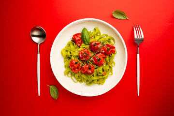 Green Tagliatelle pasta with cherry tomatoes and basil on red background, top view