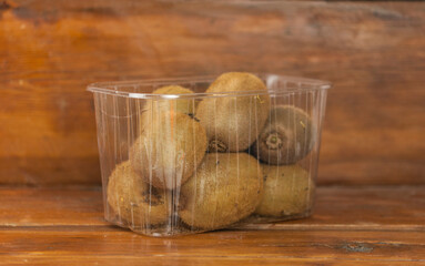 Plastic container with ripe kiwi on wood table