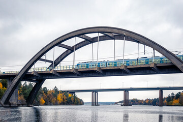 Nature autumn landscape scene with large arch concrete bridge with train crossing over calm water.