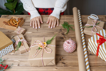 Woman s hands wrapping Christmas gift, close up. Unprepared presents on wooden background with decor elements and items, top view. Christmas or New year DIY packing Concept. Step by step.