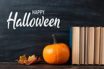 Pumpkin, fallen leaves, books and the inscription of a happy halloween. The concept of a holiday all saints' eve, greeting card.