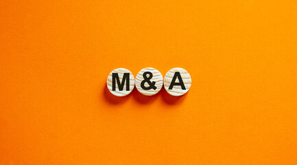 Concept word 'M and A' on wooden circles on a beautiful orange background. Business concept. Copy...